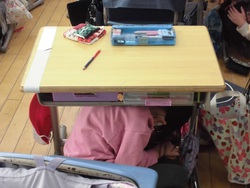 机の下に避難している児童の写真