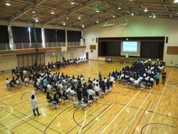 体育館に3つの学年がコの字の形に集合している写真