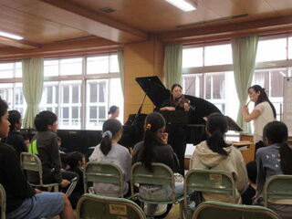 ピアノ、バイオリン、フルートの演奏を聴く児童